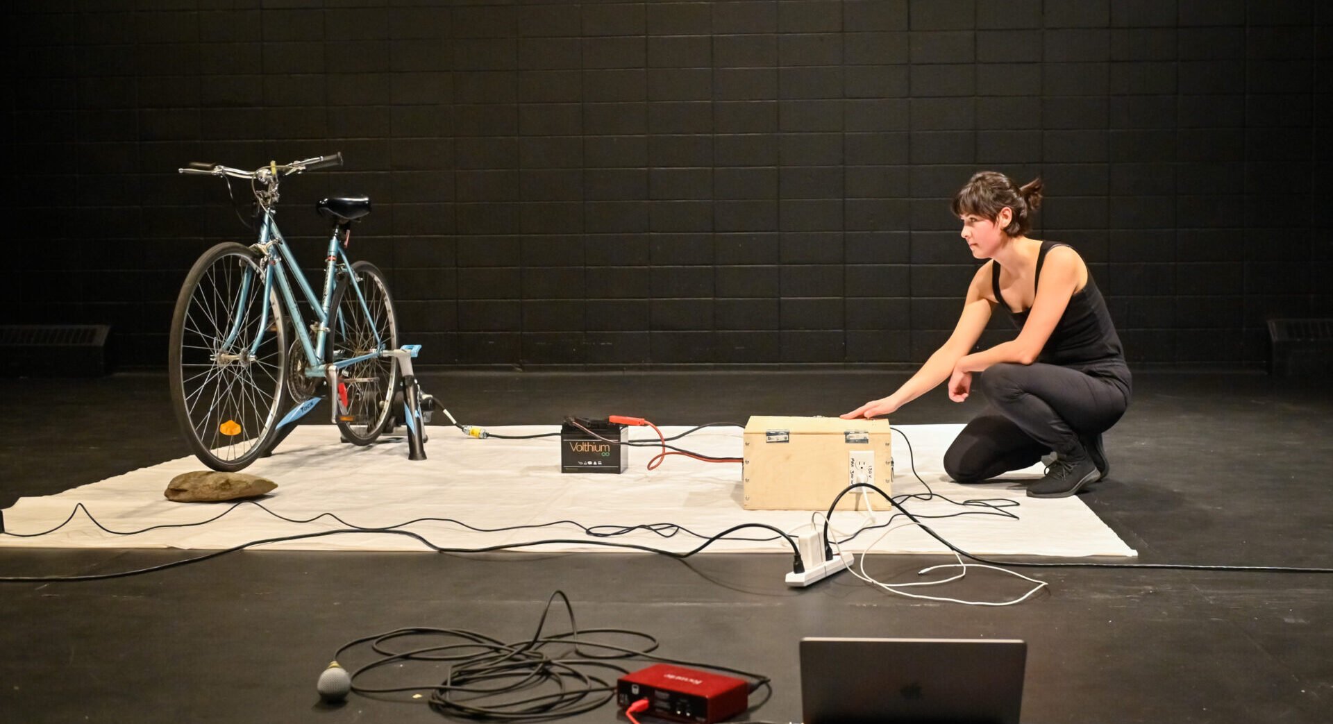 Photo features Mykalle Bienlinski on stage with tools and a bike on the far left.