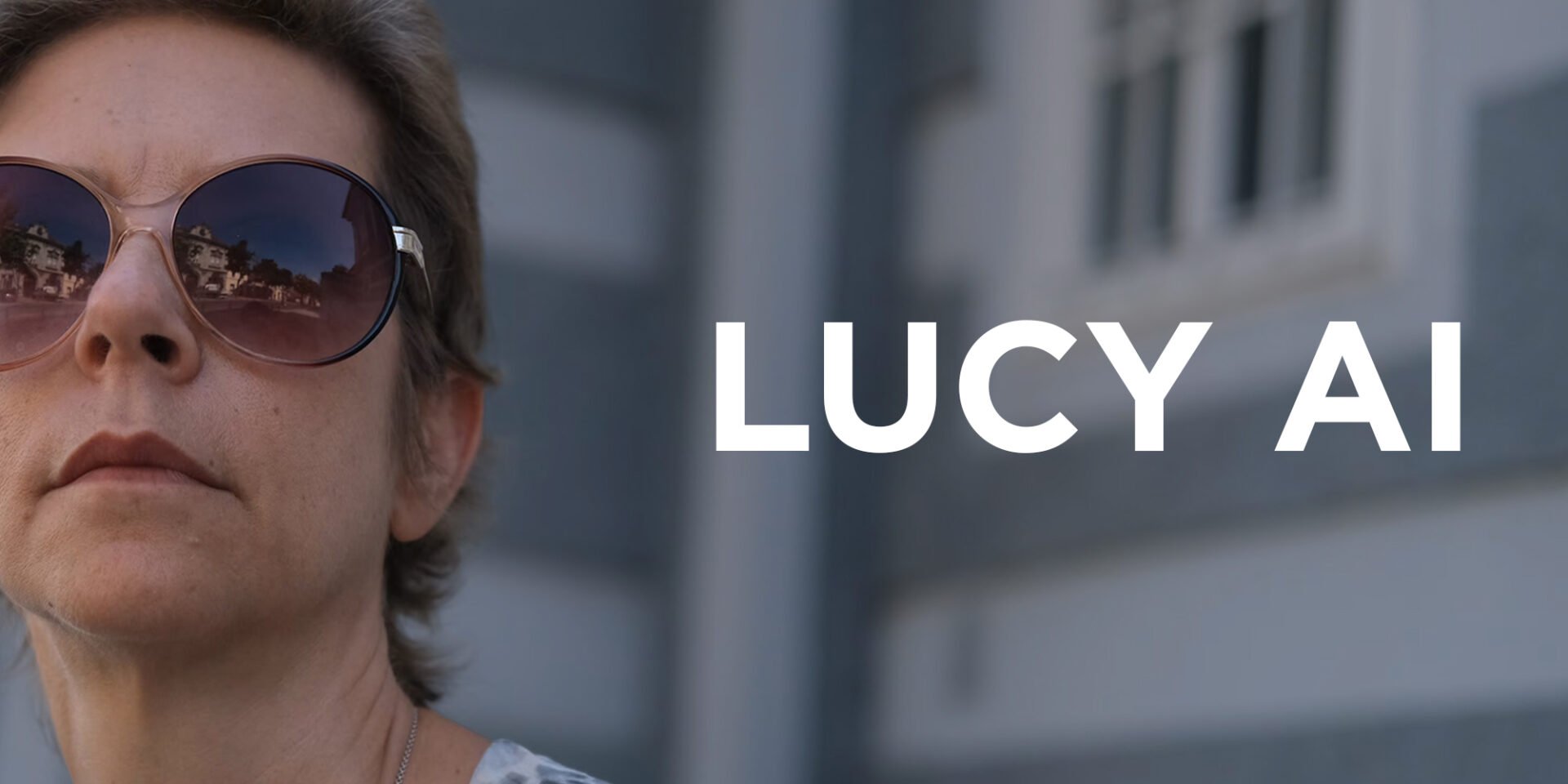 Lucy, in short hair and wearing large sunglasses, looks up into the distance.